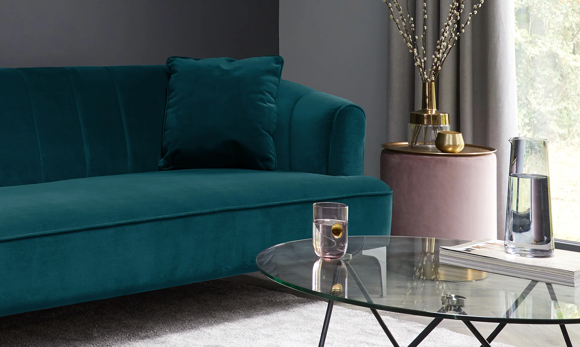 A teal sofa in velvet accentuates the textural contract between velvet and the glass coffee table